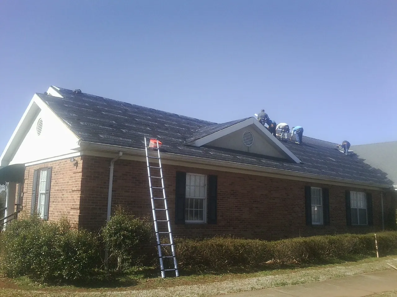 Crew tearing shingles off a brick ranch roof with a ladder set — Metal Roof Repair work by our crew in Denison